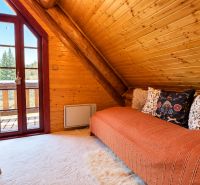 The interior of a cabin with wooden paneling, a sofa, and a view of the surrounding nature.