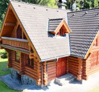 A wooden cabin in Banská Bystrica surrounded by dense forest and green lawn.