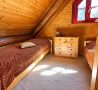 A wooden interior of a cabin with two beds and a window with a red frame.
