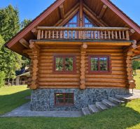 A wooden cottage in Banská Bystrica with a green lawn and a forest in the background.
