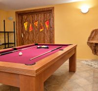 A billiard table with accessories in a cabin with warm walls and an armchair.