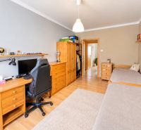 A room in a 3-room apartment with a wooden decor floor, contains a desk and a bed.