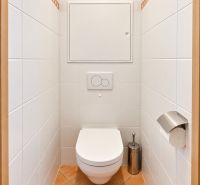 A toilet with white tiles and orange flooring in a 3-room apartment.