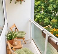 A balcony with flowers and wooden furniture in a 3-room apartment with a view of greenery.