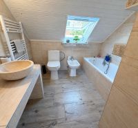 A bathroom in a family house with a bathtub, a sink, and a floor with a wooden decor.
