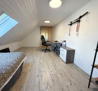 Attic room with wood-patterned flooring, a bed, and a desk in a family house.
