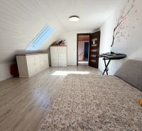 The attic of a family house with a bed, dressers, and a skylight window, flooring with a wooden decor.