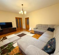 Living room with wood-patterned flooring, a large sofa, and a television in a family house.