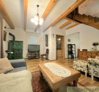 Living room in a cottage with wooden beams, wood-patterned flooring, and a stove.
