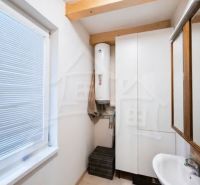 A bathroom in a cabin with a sink and a boiler, light walls and wooden beams.