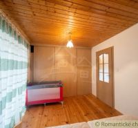 A room in a cabin with a wooden decor floor, a crib, and curtains.