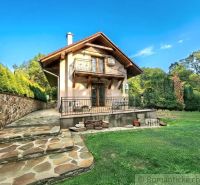 A cottage in Ružiná with a stone staircase and a lawn surrounded by greenery and a blue sky.