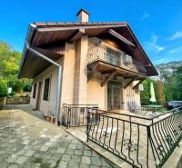 A cottage in Ružiná with a terrace and a balcony, surrounded by greenery and a blue sky.