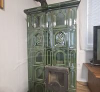Traditional green ceramic stove in the interior of a cottage with a wood-patterned floor.