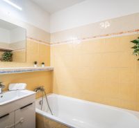 A bathroom in a 2-room apartment with light tiles and a bathtub, decorated with plants.