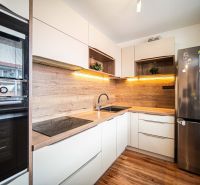 A kitchen with a wood-patterned floor, neutral cabinets, and modern appliances in a 2-room apartment.