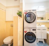 Bathroom with a washing machine, dryer, toilet, and bathtub in a 2-room apartment.