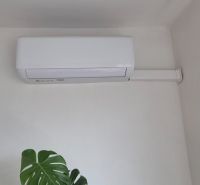 An air conditioner on the wall in a family house, next to the leaves of a plant.