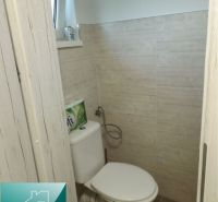 Bathroom in a cottage with a toilet, rectangular window, and wooden decor tiles.