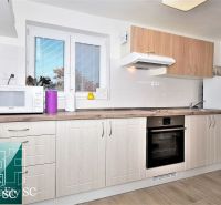 A kitchen in a cottage with white cabinets and appliances, flooring with a wood design.