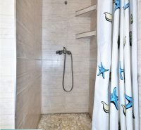 A shower corner with light tiles and a curtain with a sea motif in a cottage.