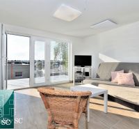 Living room of the cottage with a sofa, rattan chair, and glass doors to the terrace.