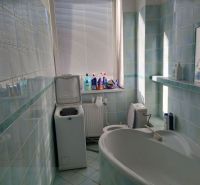 A bathroom with a bathtub and a washing machine, tiled with light blue tiles.