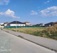 Residential plots in Senec surrounded by houses and greenery under a blue sky.