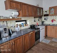 A kitchen in a family house with appliances, rustic cabinets, and a wood-patterned floor.