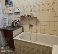 A bathroom in a family house with a bathtub, a washing machine, and tiles with a floral pattern.