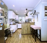 A kitchen in a 2-room apartment with a wooden decor floor and white cabinets.