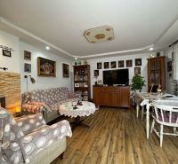 Living room with wood-patterned flooring in a two-room apartment, decorated with paintings and a fireplace.