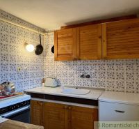 A kitchen in a cottage with wooden cabinets and tiles with a blue pattern.