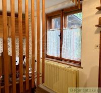 Interior of a cabin with wooden elements, a kitchen, and a window with curtains.