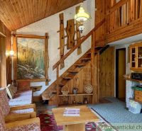 A cottage with wooden decor, armchairs, a painting on the wall, and a staircase leading to the upper floor.