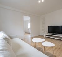 Living room in a two-room apartment with a wooden decor floor and white furniture.