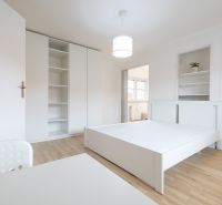 A bright bedroom with white furniture and a floor with a wood decor, in a two-room apartment.