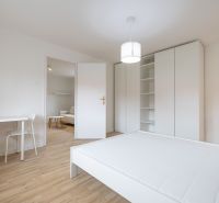 A room of a 2-room apartment with white furniture, a bed, and a floor with a wood decor.