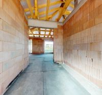 An unfinished interior of a family house with brick walls and visible wooden roof structure.