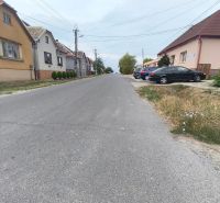 A street in Mikušovce with family houses and parked cars on both sides.