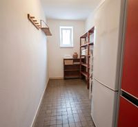 A narrow room in a family house with a refrigerator, shelves, a window, and a clothes hanger.