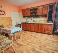 A kitchen in a family house with a wooden decor floor, a wooden kitchen unit, and a table with chairs.