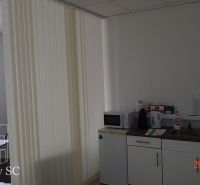 Office kitchenette with appliances, cabinets, and vertical blinds.