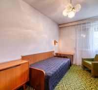 A bedroom in a family house with simple furniture, a green armchair, and a patterned carpet.