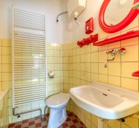 A bathroom in a family house with tiled flooring and yellow tiles, with red accessories brightening up the space.