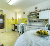 A kitchen in a family house with white furniture and a dining table with fruit.