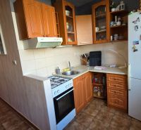 A kitchen in a 3-room apartment with wooden cabinets, a gas stove, and a white refrigerator.