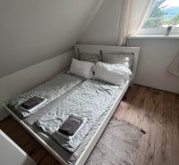 A bedroom in a cabin with a bed, wooden decor flooring, and a window.