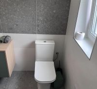 Bathroom section of the cottage with a toilet, sink, and tiles in gray decor.