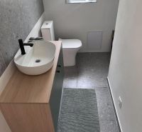 A bathroom in a cabin with a toilet, a sink on a wooden cabinet, and a window for natural light.